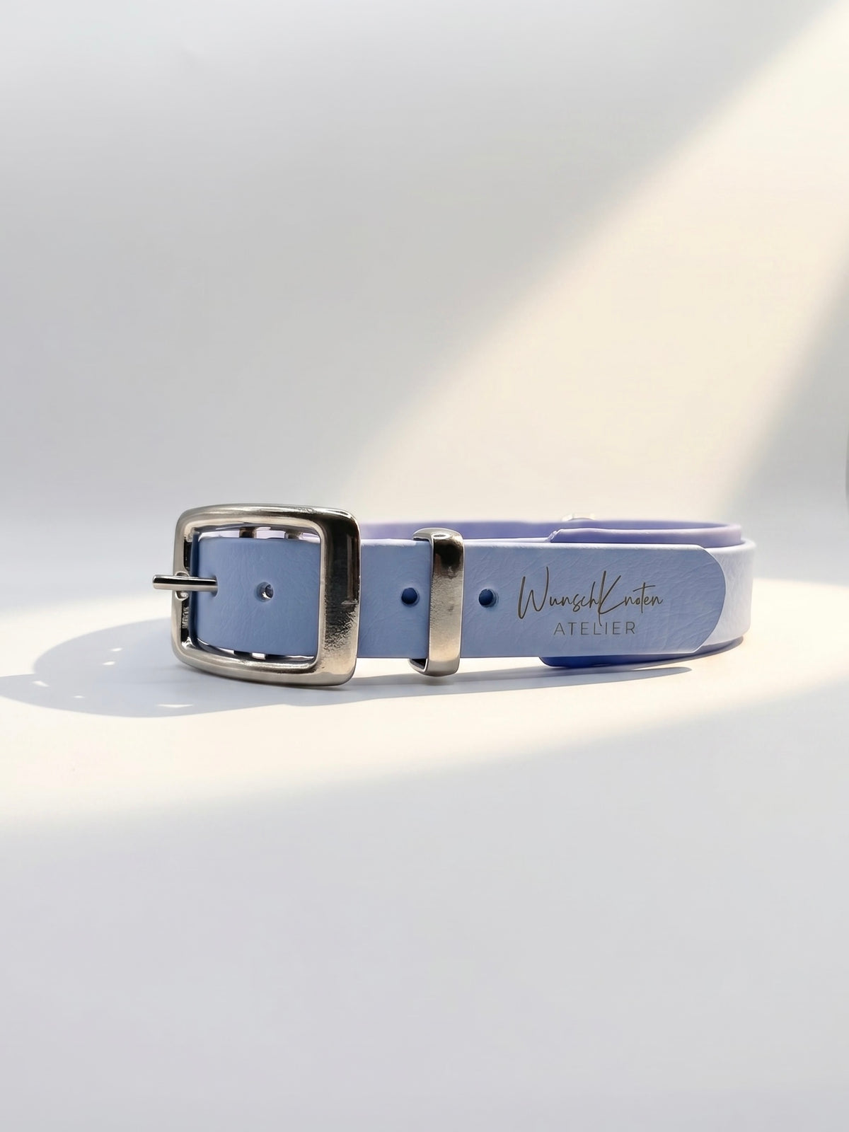 Detailaufnahme des WunschKnoten Atelier Logos auf einem handgefertigten BioThane Hundehalsband in Polar Blau und Periwinkle mit silbernen Beschlägen – hochwertige Verarbeitung und individuelles Design