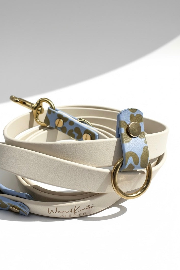 Detailaufnahme der Leoparden Hundeleine aus BioThane in Arctic Wolf und Polar Blau mit goldfarbenen Messingbeschlägen, Fokus auf hochwertige Verarbeitung und feine Details der Leine. Handgefertigte BioThane Hundeleine im Leoparden Design mit stabilen Karabinern, sauber gearbeiteten Verbindungsstellen und individuell einstellbaren Verstellmöglichkeiten. Personalisierbare Hundeleine mit wählbarer Länge, anpassbarer Breite und frei auswählbarer Beschlagfarbe. Strapazierfähiges, wasserfestes und pflegeleichtes 