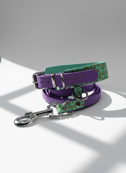 Leoparden Hundeset aus BioThane bestehend aus Hundehalsband und Hundeleine im Farbdesign Caribbean Grün und Amethyst Orchid mit goldfarbenen Messingbeschlägen, Frontansicht des personalisierbaren Hundesets im Leo Design. Handgefertigtes BioThane Hundeset mit individueller Namensgravur oder Logo Gravur möglich. Halsband wahlweise als verstellbares Halsband oder Zugstopp Halsband erhältlich. Breite, Beschlagfarbe, Leinenlänge sowie Verstellmöglichkeiten frei konfigurierbar. Robustes, wasserfestes und pflegele