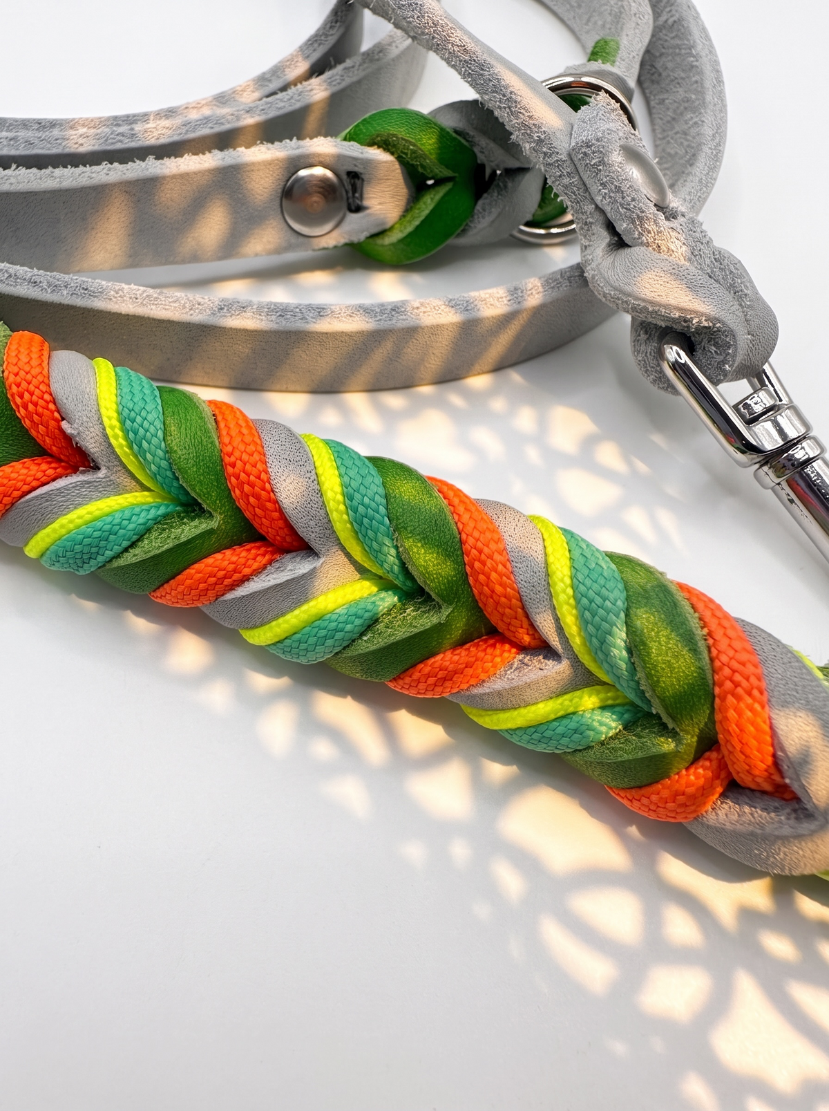 Hundeleine geflochten aus Leder in den Farben silbergrau und grün. Geflochten mit orange, gelb und grünen Details. Details der Flechtung 